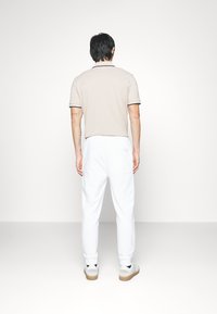 Beige poloshirt met zwarte kraagafwerking, gecombineerd met witte sweatpants. Heeft een eenvoudig ontwerp met een ontspannen pasvorm en een zachte textuur.