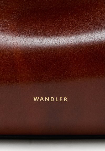 Καφέ δερμάτινη επιφάνεια με λεία υφή, με μια χρυσή σφραγισμένη στάμπα "WANDLER" κοντά στο κάτω μέρος.