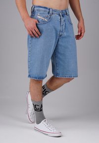 Light blue denim shorts with a loose fit, faded texture, five pockets, and stitched details. Worn with gray socks and white sneakers.