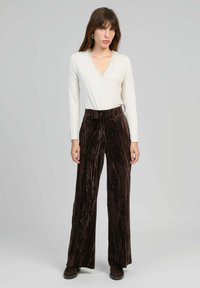 Un haut crème à manches longues et décolleté en V associé à un pantalon large en velours marron foncé avec une texture verticale subtile. Des bottines brunes à la cheville complètent le look.