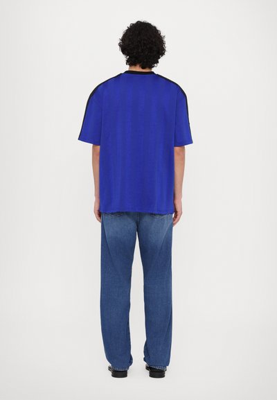 Blauwe oversized T-shirt met korte mouwen, met zwarte accenten op de schouders. Gecombineerd met losse blauwe jeans.