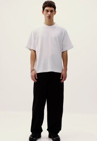 Tricou alb oversized cu mâneci scurte, asortat cu pantaloni negri largi și pantofi negri. Design simplu, fără modele sau logo-uri vizibile.