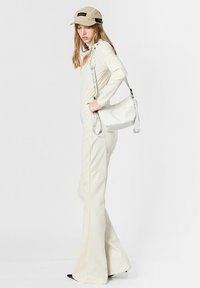 Bolso blanco de hombro con acabado texturizado, correa gris ajustable, combinado con una blusa cremosa de manga larga y pantalones acampanados de talle alto.