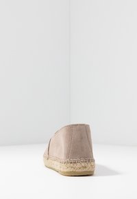 Beżowy zamszowy espadryl z płaską jucie podeszwą i przeszyciami. Widok z tyłu ukazuje gładką cholewkę i zakrzywiony fason obcasa.