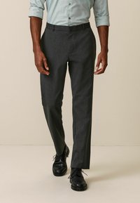 Un pantalon gris foncé, ajusté, avec une texture lisse et une coupe droite. Porté avec une chemise à boutons bleu clair et des chaussures noires.