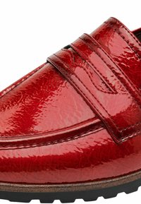 Red patent leather loafer with a smooth, shiny finish, featuring a decorative strap and textured detailing, set on a black rubber sole.