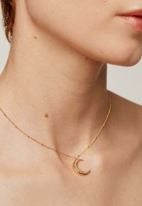 Collar de cadena de oro con un colgante de media luna adornado con cristales transparentes, sobre un fondo de piel suave.