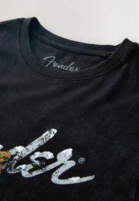 Czarny bawełniany T-shirt z okrągłym dekoltem, z nadrukiem podniszczonego białego logo "Fender" na przodzie. Miękka faktura.