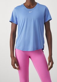 Modrá sportovní tričko Nike s krátkým rukávem, kulatým výstřihem a malým bílým logem. Kombinované s přiléhavými růžovými legínami s bočním švem.