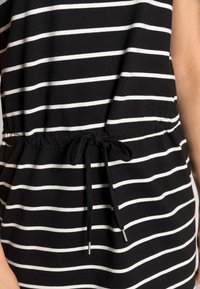 Haut rayé noir et blanc avec une texture douce. Dispose d'une taille élastique avec un cordon de serrage à nouer et des embouts en métal.