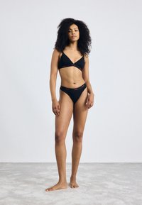 Zwart bikini-set met een driehoekige beha en high-waisted slipjes met rode "HUGO" branding. Zachte stof met een minimalistisch ontwerp.