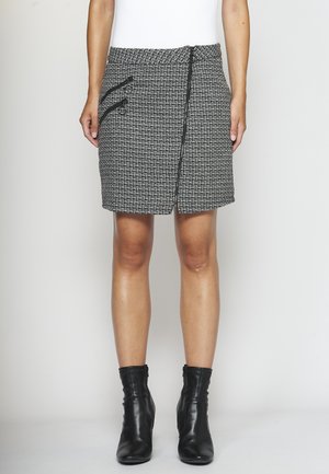 Falda tejida en blanco y negro con cintura alta, dos bolsillos laterales con cremallera y un diseño de solapa en la parte frontal. Combinada con botas negras hasta el tobillo.
