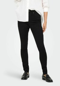 Mustad teksad musta värviga, millel on sile tekstuur ja keskmise kõrgusega vöökoht, mida täiendab valge nööpidega särkjakk ning mustad naiste kingad nupudega.