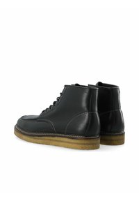 Botas de cuero negro hasta el tobillo con un acabado suave, punta redonda y seis ojales. Suela de goma gruesa con detalles de costura en contraste.