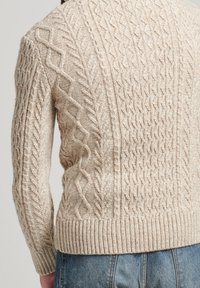 Beige gestrickter Pullover mit strukturierten Kabelmustern, geripptem Saum und enganliegenden Ärmeln. Auffällige Diamant- und Drehdesigns überall.