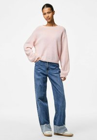 Ljust rosa stickad tröja med vid halsringning och långa ärmar, kombinerad med högmidjade blå jeans med fransade avslut och kontrasterande muddar.