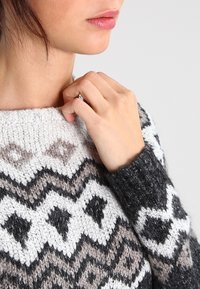 Maglione lavorato a maglia con un design a motivi, caratterizzato da forme geometriche in nero, bianco e grigio. Collo a giro e tessuto strutturato.