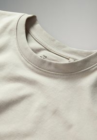 Hellbeige Baumwoll-T-Shirt mit klassischem Rundhalsausschnitt und subtiler Textur, mit eng zusammen genähtem Detail am Kragen.