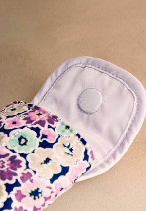 Absorbant reutilizabil din material textil cu un clapetă care afișează un nasture alb, având un model floral colorat pe țesătură.