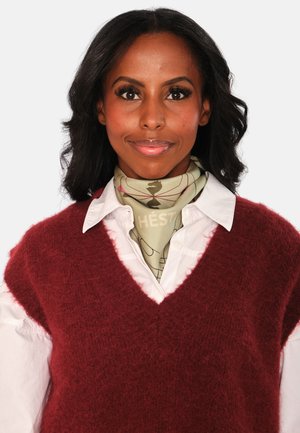 Bordo, pötu vesta üle valge kraega särgi, millele on lisatud heledat rohelist sall, millel on muster. Sile tekstuur ja V-kaelus.