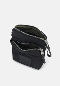 Czarna torba nylonowa z dwiema zamykanymi komorami; srebrne okucia; posiada teksturowany naszywkę z nazwą marki. Gładka podszewka wewnętrzna.