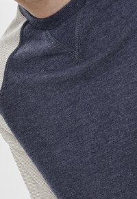 Granatowa koszula z długim rękawem z teksturowanym, jasnoszarym panelem na ramieniu. Miękka tkanina z okrągłym dekoltem i rękawami raglan.