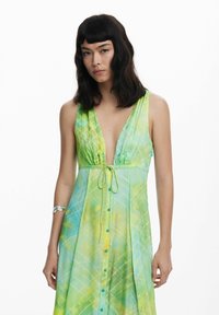 Abito verde e giallo a fantasia con scollatura a V profonda, coulisse regolabile in vita e chiusura frontale con bottoni. Tessuto leggero.