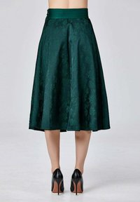 Jupe en satin vert avec un motif floral, au design évasé, longueur genou, comportant une ceinture texturée. Portée avec des talons hauts noirs.