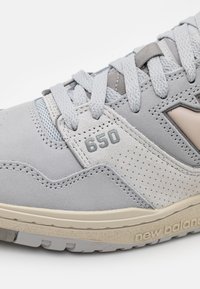 Světle šedé tenisky New Balance se surovou a síťovanou textilií, texturovaným svrškem, perforovanými detaily a krémovou podrážkou.