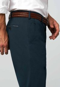 Marineblaue Hosen mit glatter Textur, ausgestattet mit einem geflochtenen, braunen Ledergürtel, seitlichen Taschen und einem Knopfdetail auf der Rückseite.