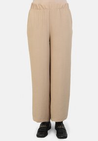 Pantaloni ampi beige, con texture e cintura elastica. Tessuto morbido, senza tasche. Abbinati a scarpe nere con accessori dorati.