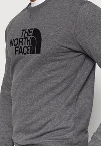 Grauer Sweatshirt mit Rundhalsausschnitt aus weichem Stoff, mit schwarzem Logodruck auf der Vorderseite und gerippten Bündchen mit Nahtdetails.