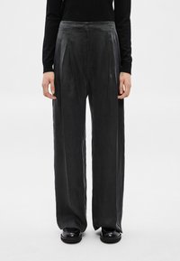 Calças de cintura alta e perna larga em cinzento escuro, com pregas, textura suave e corte ajustado, combinadas com sapatos pretos.