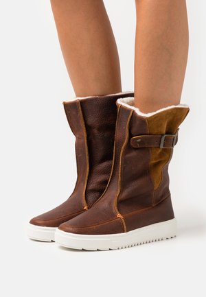 Brown leather and suede mid-calf boots with white rubber soles, faux fur lining, and a side buckle accent. Features contrast stitching.