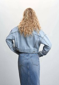 Giacca in denim blu chiaro con un design corto, caratterizzata da cuciture visibili e grandi tasche, abbinata a una gonna a vita alta coordinata.