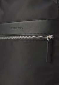 Black bag features smooth textile material with a matte finish. It has a zippered pocket and embossed "Pier One" branding. Silver hardware accents.