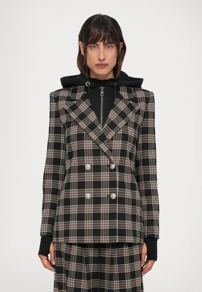 Plaid double-breasted blazer in black, white, and orange with metallic buttons, sharp lapels, and structured shoulders. Worn over a black hoodie.