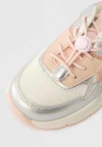  Κρέμα και ροζ αθλητικά παπούτσια με ασημένια σχέδια, λεπτομερή ραφή, δίχτυ και ροζ ελασμένα κορδόνια που ασφαλίζουν με έναν στρογγυλό πλαστικό κομβίο.