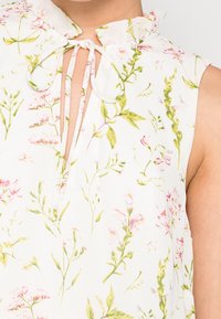 Floral blouse with a ruffled collar, featuring a white fabric adorned with pink and green botanical patterns, and a keyhole neckline detail.