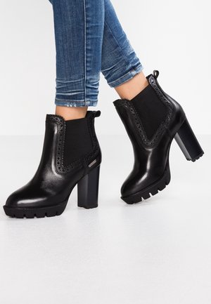 Bottines en cuir noir avec une finition texturée, panneaux latéraux élastiques, couture décorative, et un talon chunky avec une semelle robuste.