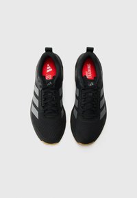 Black athletic shoes with mesh upper, reflective grey stripes, red insoles labeled "ADIDAS TRAINING," and rubber outsole.