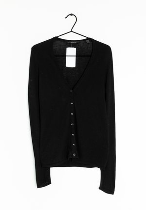 Schwarze langärmelige Strickjacke mit V-Ausschnitt, ausgestattet mit einer Knopfleiste auf der Vorderseite und einer sanften Textur. Hängt an einem schwarzen Haken.