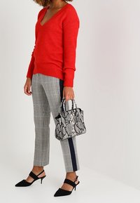 Pull v-neck rouge, pantalon à carreaux gris avec une rayure marine sur le côté, chaussures noires à talons carrés et un petit sac à main en peau de serpent.