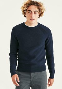 Pull en tricot bleu marine avec un col rond, des manches raglan texturées et des bords-côtes aux manches et à l'ourlet. Matière lisse et coupe ajustée.