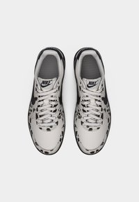 Nike superge z bež in črnim leopardjim vzorcem, teksturiranim sivim jezikom ter belimi vezalkami in črnim logotipom Swoosh.