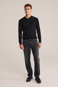 Črn pulover s V-izrezom, oprijetega kroja, z dolgimi rokavi. Nosi se z temno sivo jeansom in črnimi čevlji. Preprost, ravno teksturiran, z minimalnimi detajli.