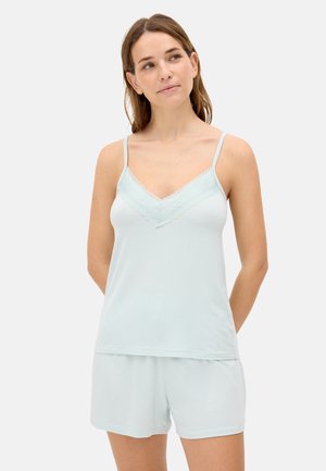 Mujer de pie con las manos detrás de la espalda, vistiendo un camisón azul claro con encaje y shorts a juego, sobre un fondo liso.