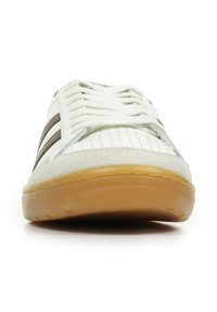 Sneaker bianca con tomaia perforata, strisce marroni e particolari in suede grigio. Suola in gomma arrotondata con fondo testurizzato. Lacci visibili sopra.