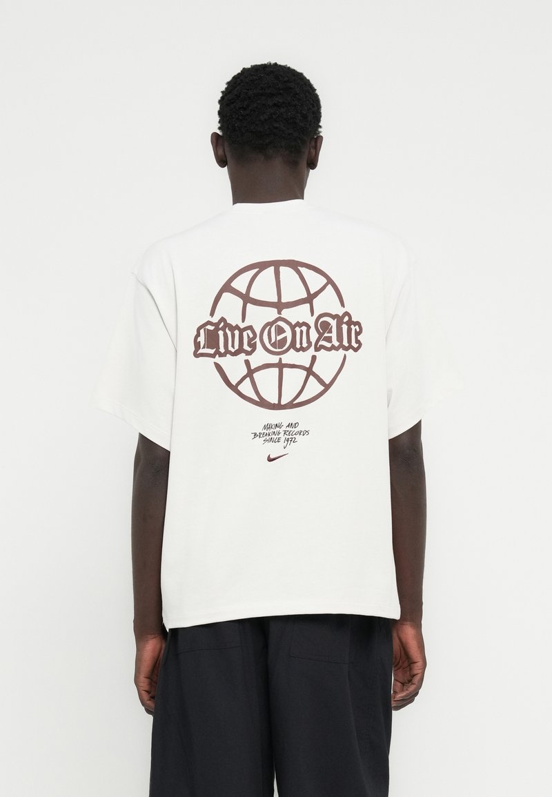 Λευκό βαμβακερό t-shirt με καφέ γραφικό ενός γήινου σφαίρας και το κείμενο "Live On Air", στρογγυλή λαιμόκοψη, κοντά μανίκια και άνετη εφαρμογή.