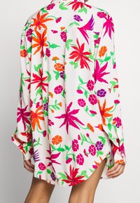 Blůza s dlouhým rukávem z lehké látky, s výrazným květinovým vzorem růžových, oranžových a zelených květů na bílém pozadí.